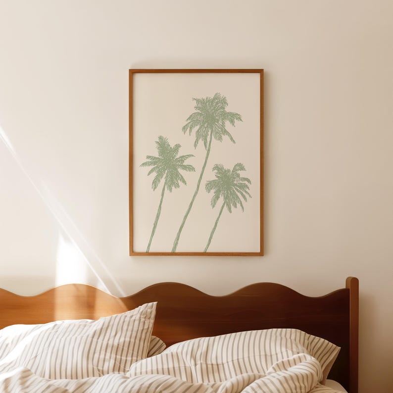 Puede incluir: Un cuadro enmarcado con tres palmeras estilizadas en un suave tono verde sobre un fondo crema. La obra de arte est&aacute; encerrada en un marco de madera marr&oacute;n c&aacute;lido. El cuadro cuelga sobre una estructura de cama de madera con ropa de cama a rayas.