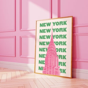 Pu&ograve; includere: Una stampa incorniciata con uno sfondo rosa e bianco che presenta un'illustrazione rosa del Chrysler Building a New York City. Le parole "NEW YORK" sono ripetute in testo verde.