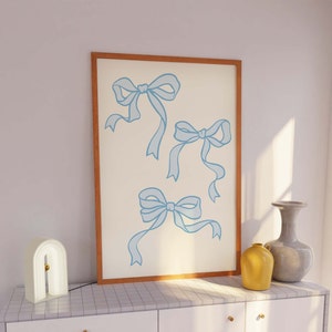 May include: A framed print with a white background and three blue ribbon bows. The bows are drawn in a simple, minimalist style.