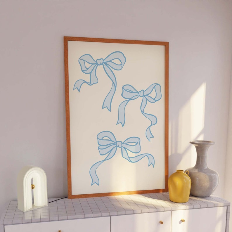 May include: A framed print with a white background and three blue ribbon bows. The bows are drawn in a simple, minimalist style.