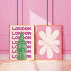 May include: Two framed prints on a pink wall. The print on the left features a green image of Big Ben with the word "LONDON" repeated in pink. The print on the right features a white stylized flower on a pink background.