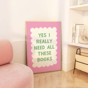 May include: A pink framed poster with a white background and green text that reads "Yes I Really Need All These Books". The text is inside a white scalloped border.