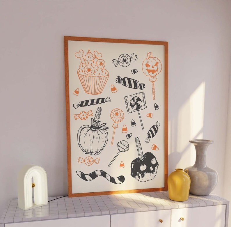 K&ouml;nnte beinhalten: Ein gerahmter Druck mit Halloween-Motiv, der verschiedene schwarze und orangefarbene Illustrationen von S&uuml;&szlig;igkeiten, Cupcakes und K&uuml;rbissen zeigt. Der Druck ist auf wei&szlig;em Hintergrund mit einem Holzrahmen.
