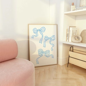 May include: A framed print with a white background and three blue ribbon bows in different positions. The print is hanging on a white wall.