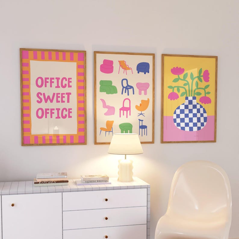 May include: Three framed art prints. The left print has the text "OFFICE SWEET OFFICE" in pink on a cream background, framed with orange and pink stripes. The middle print features colorful chair illustrations. The right print shows a vase with flowers.