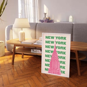 Pu&ograve; includere: Una stampa incorniciata con un'illustrazione rosa e verde di un grattacielo. Il testo "NEW YORK" &egrave; ripetuto in lettere verdi su uno sfondo rosa.