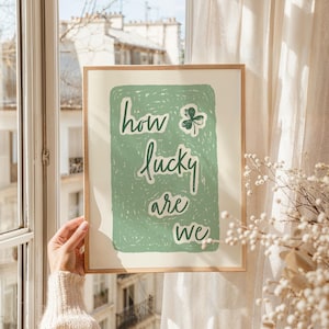 May include: A framed print with a green background and white text that reads "how lucky are we". A green shamrock is in the upper right corner of the print.