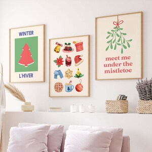 May include: Three framed prints with a winter theme. The first print has a red Christmas tree with the words "Winter" and "L'Hiver" on it. The second print has a collection of Christmas icons, including a Christmas tree, a stocking, a candy cane, and a present. The third print has a green mistletoe with the words "Meet me under the mistletoe" on it.