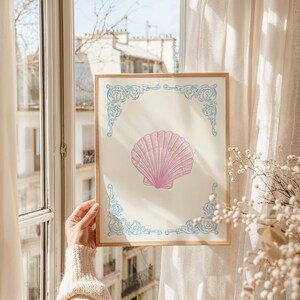 Puede incluir: Una impresi&oacute;n enmarcada con una ilustraci&oacute;n de concha rosa sobre fondo blanco. El marco tiene un dise&ntilde;o ornamentado azul y blanco.