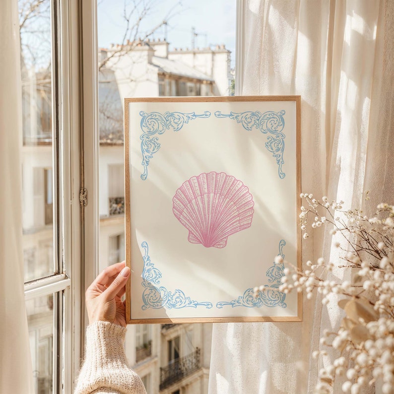 Puede incluir: Una impresi&oacute;n enmarcada con una ilustraci&oacute;n de concha rosa sobre fondo blanco. El marco tiene un dise&ntilde;o ornamentado azul y blanco.