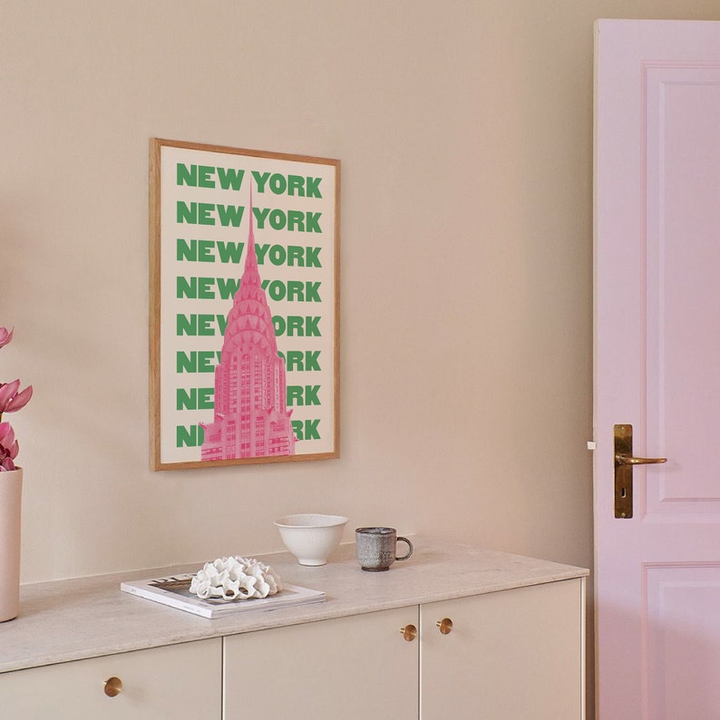 Pu&ograve; includere: Una stampa incorniciata con un'illustrazione rosa del Chrysler Building a New York City. Il testo "NEW YORK" &egrave; ripetuto in lettere verdi lungo il lato della stampa.