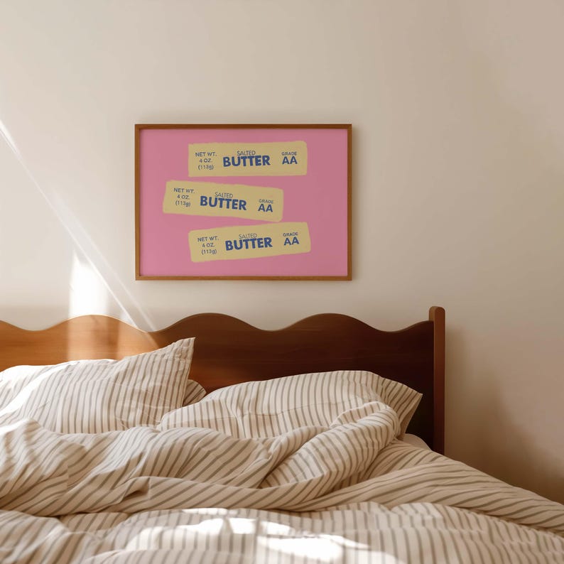 Peut inclure: Une &oelig;uvre d'art encadr&eacute;e repr&eacute;sentant trois &eacute;tiquettes de beurre stylis&eacute;es sur fond rose. Les &eacute;tiquettes indiquent "SALTED BUTTER AA" et "NET WT 4 oz (113g)". L'&oelig;uvre est affich&eacute;e au-dessus d'un lit avec une literie &agrave; rayures.