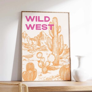 May include: A framed print with the text "WILD WEST" in pink lettering. The print features a desert landscape with a large cactus and smaller cacti in orange.