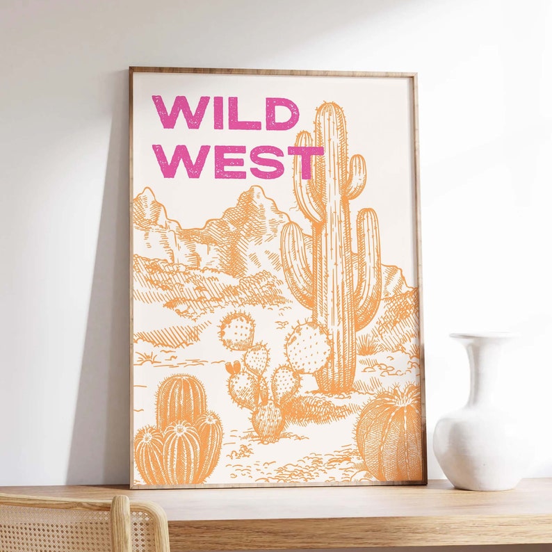 May include: A framed print with the text "WILD WEST" in pink lettering. The print features a desert landscape with a large cactus and smaller cacti in orange.