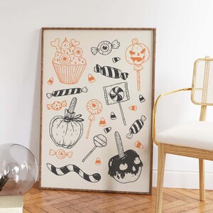 K&ouml;nnte beinhalten: Eine Schwarzwei&szlig;illustration von Halloween-Leckereien, darunter ein Cupcake, Candy Corn, Lutscher und ein Karamellapfel. Die Illustration ist auf wei&szlig;em Hintergrund und in einem braunen Rahmen gerahmt.