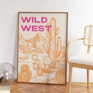 May include: A framed print with a desert landscape featuring a large cactus and the text "WILD WEST" in pink lettering.