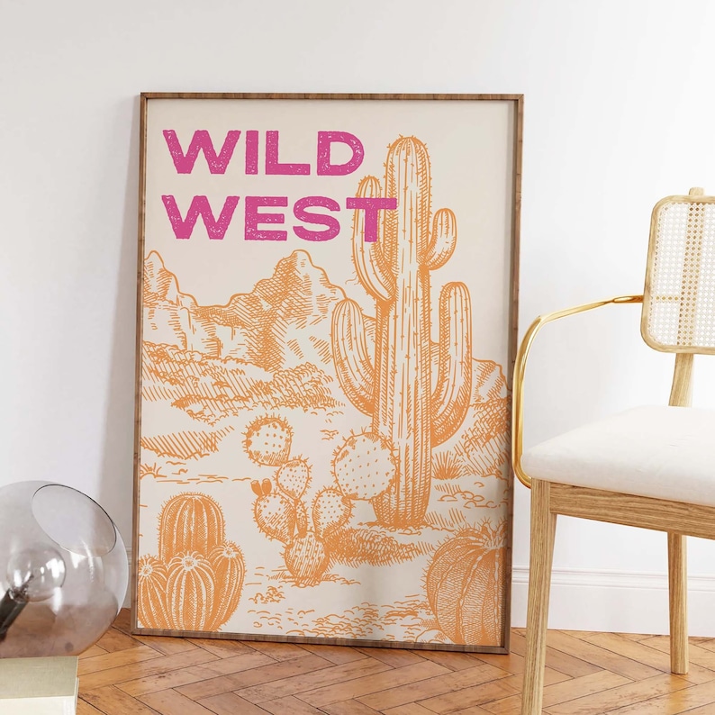 May include: A framed print with a desert landscape featuring a large cactus and the text "WILD WEST" in pink lettering.