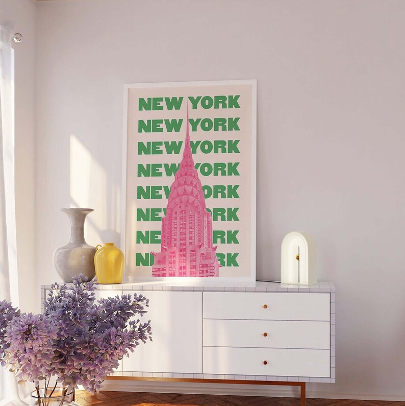 Pu&ograve; includere: Una stampa incorniciata bianca con un'illustrazione rosa e verde del Chrysler Building a New York City. La stampa riporta le parole "NEW YORK" ripetute in testo verde.