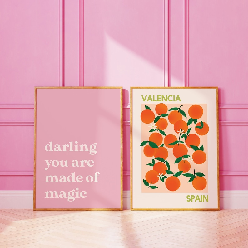 May include: Two framed prints with a pink background. The left print has the text "darling you are made of magic". The right print has a pattern of orange fruit with green leaves and white flowers. The text "VALENCIA SPAIN" is at the bottom of the print.