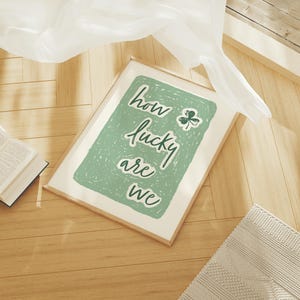 May include: A framed print with a green background and white text that reads "how lucky are we". A green shamrock is in the upper right corner of the print.