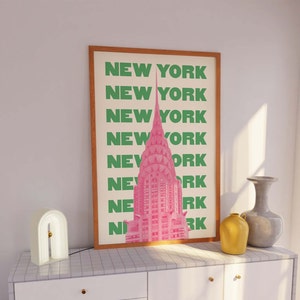 Pu&ograve; includere: Una stampa incorniciata con un'illustrazione rosa del Chrysler Building a New York City. Il testo "NEW YORK" &egrave; ripetuto in lettere verdi lungo il lato della stampa.