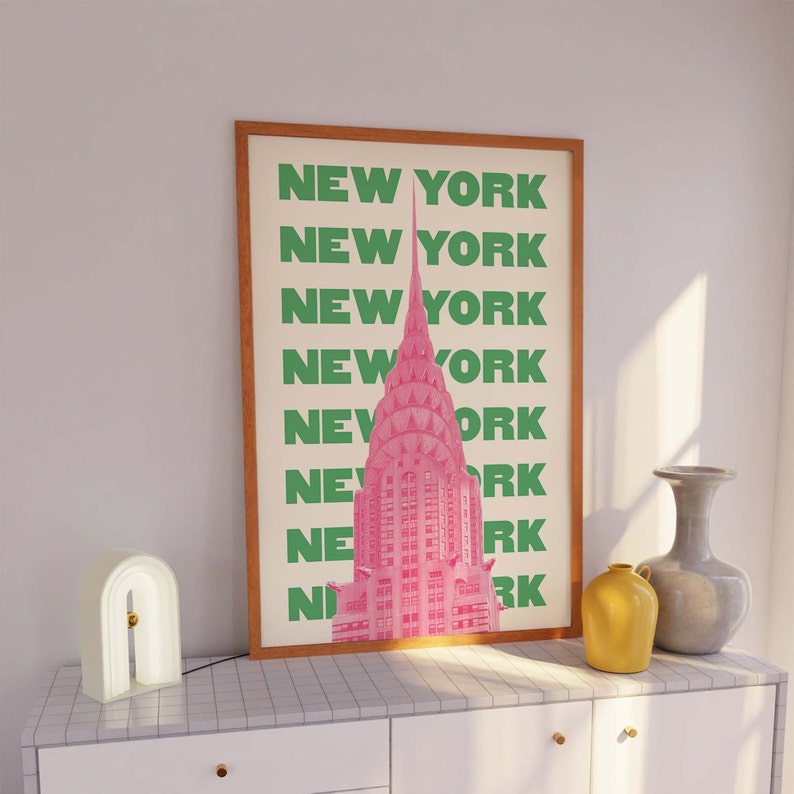 Pu&ograve; includere: Una stampa incorniciata con un'illustrazione rosa del Chrysler Building a New York City. Il testo "NEW YORK" &egrave; ripetuto in lettere verdi lungo il lato della stampa.