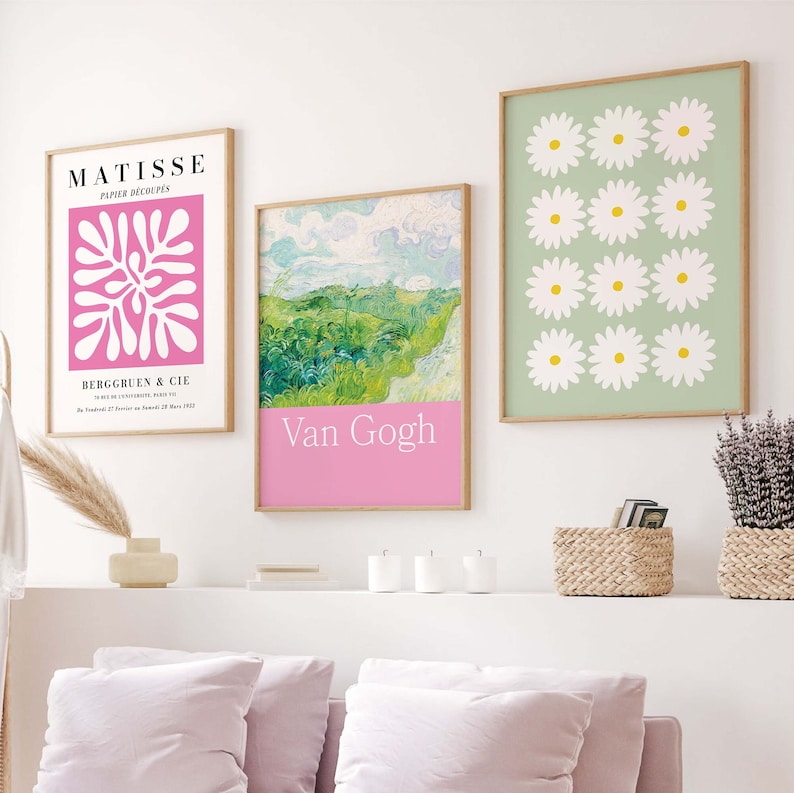 May include: Three framed art prints on a white wall above a white shelf with three white candles and a wicker basket. The prints are of a pink Matisse paper cut-out, a green landscape by Van Gogh, and a green background with white daisies.