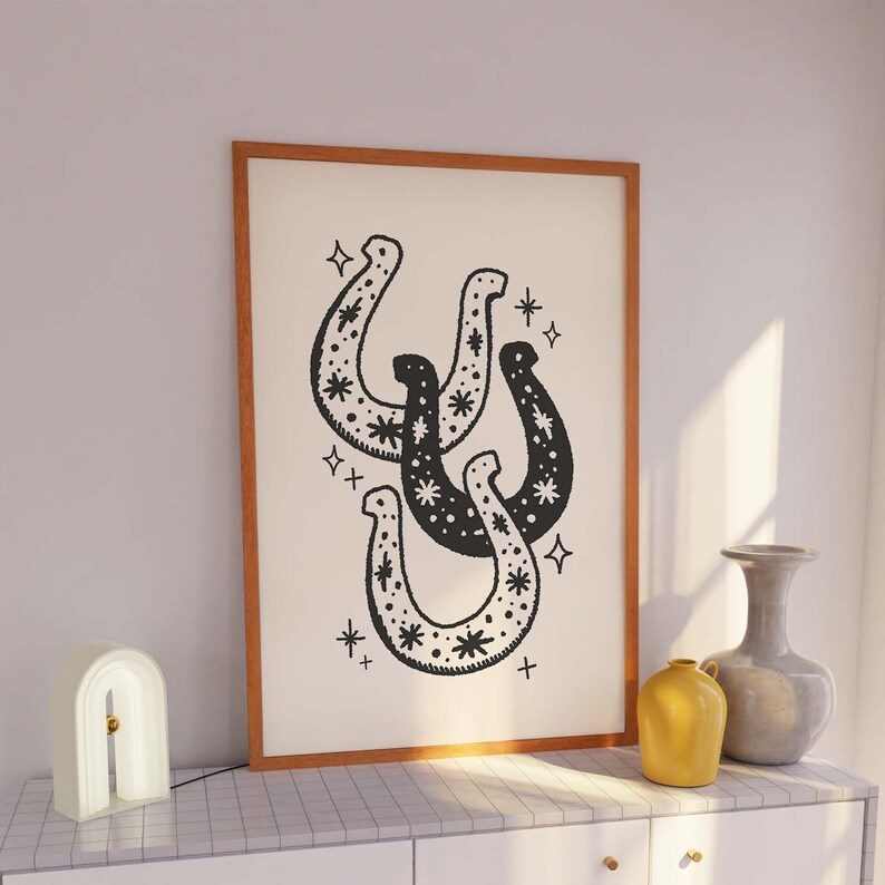 May include: A framed print with a black and white illustration of three stylized horseshoes with a star pattern. The horseshoes are arranged in a stacked formation.