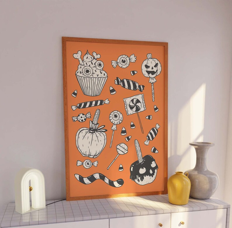 May include: A framed print with an orange background and black and white illustrations of Halloween treats, including cupcakes, candy corn, lollipops, and candy apples.