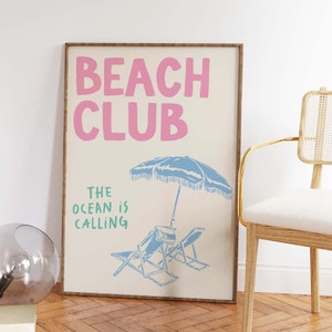 Pu&ograve; includere: Un poster beige con il testo "Beach Club" in rosa e "The ocean is calling" in verde. Il poster presenta un ombrellone da spiaggia blu e due sdraio blu.