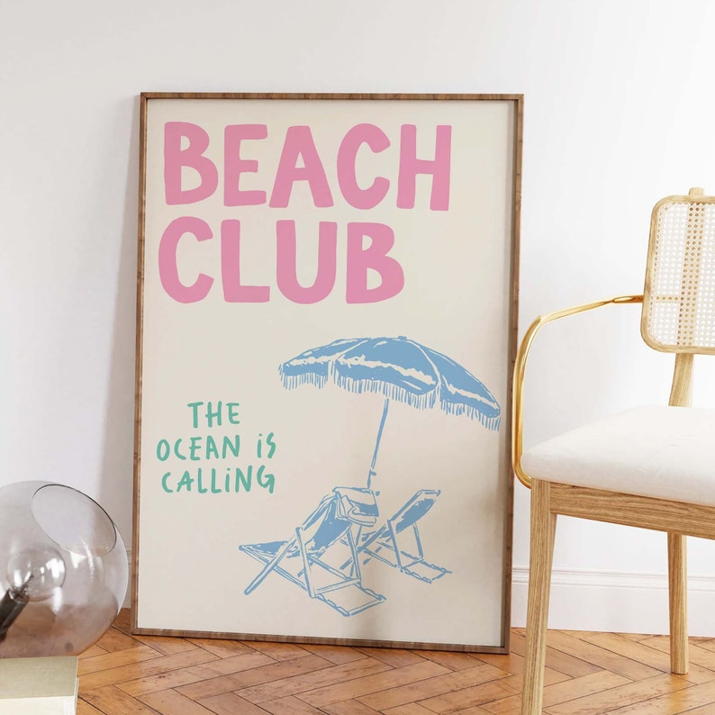Pu&ograve; includere: Un poster beige con il testo "Beach Club" in rosa e "The ocean is calling" in verde. Il poster presenta un ombrellone da spiaggia blu e due sdraio blu.