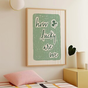 May include: A framed print with a green background and white text that reads "how lucky are we" with a four-leaf clover graphic.