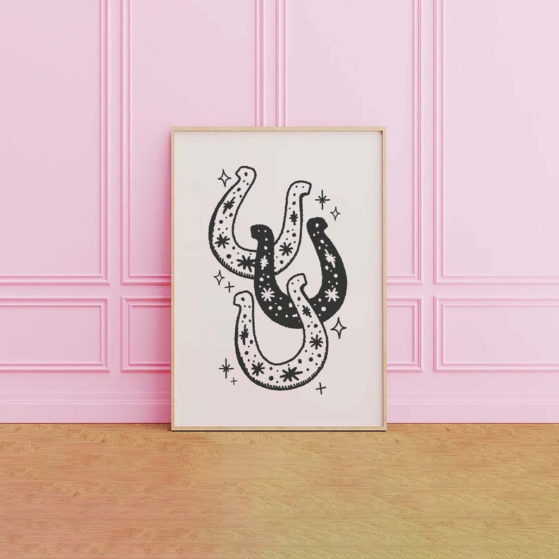May include: A black and white print of three horseshoes with a star pattern. The horseshoes are arranged in a stack with the top horseshoe facing up. The background is white.