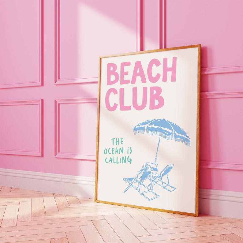 Pu&ograve; includere: Una stampa incorniciata con il testo "Beach Club" in lettere rosa e "The ocean is calling" in lettere verdi. La stampa presenta un ombrello da spiaggia blu e due sedie a sdraio.