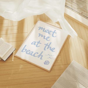Pode incluir: Uma impress&atilde;o emoldurada com fundo branco e texto azul que diz "Meet me at the beach" com uma pequena concha azul e linhas onduladas por baixo.