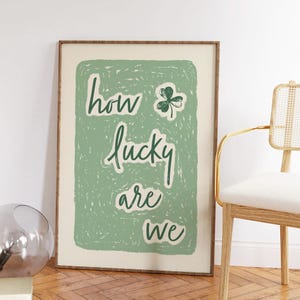 May include: A green and white poster with the text "how lucky are we" in a green cursive font. A green four-leaf clover is above the word "how".