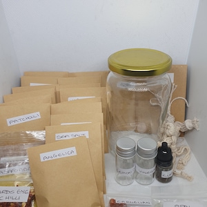 Könnte beinhalten: Eine Sammlung von Artikeln für Bastelarbeiten oder Rituale, darunter ein großes Glas mit goldenem Deckel, kleine Glasflaschen, braune Papiertüten mit Etiketten und kleine Beutel mit Kristallen.