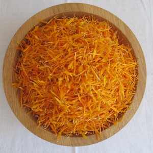 Pu&ograve; includere: Una ciotola di legno piena di petali di calendula essiccati arancioni.