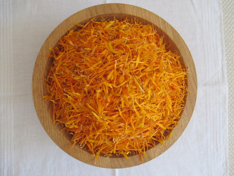 Pu&ograve; includere: Una ciotola di legno piena di petali di calendula essiccati arancioni.