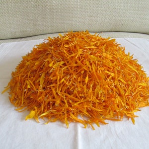 Pu&ograve; includere: Un mucchio di petali di calendula arancioni secchi su una superficie bianca.