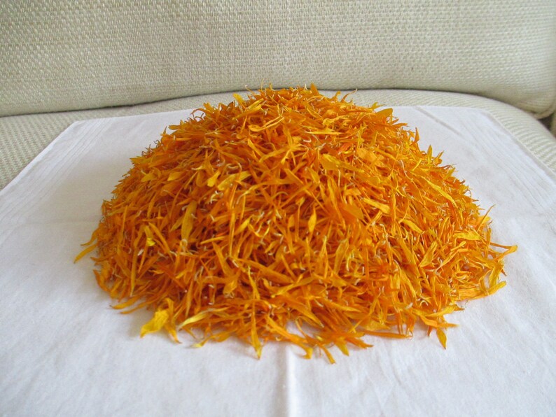 Pu&ograve; includere: Un mucchio di petali di calendula arancioni secchi su una superficie bianca.