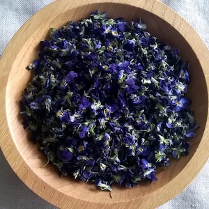 May include: A wooden bowl filled with dried violet petals. The petals are a deep purple colour and have a delicate, fragrant aroma.