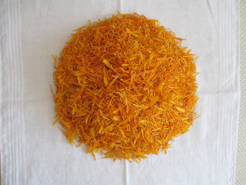 Pu&ograve; includere: Un mucchio di petali di calendula arancioni secchi su una superficie bianca.