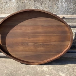 Puede incluir: Bandeja ovalada de madera para servir con asas integradas. La bandeja es de madera marr&oacute;n oscuro y tiene un acabado liso y pulido. La bandeja mide aproximadamente 61 cm de largo y 41 cm de ancho, ideal para servir alimentos o exhibir objetos decorativos.