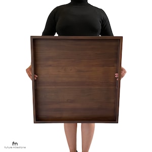 May include: A large, rectangular wooden serving tray with a dark brown finish. The tray has a smooth surface and is held by a person.