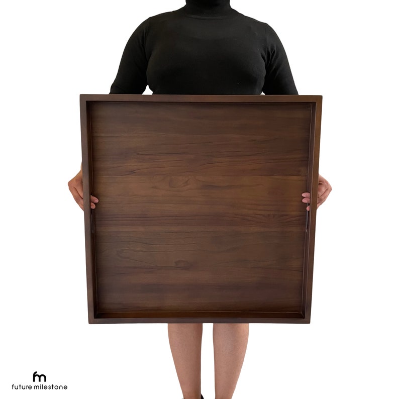May include: A large, rectangular wooden serving tray with a dark brown finish. The tray has a smooth surface and is held by a person.
