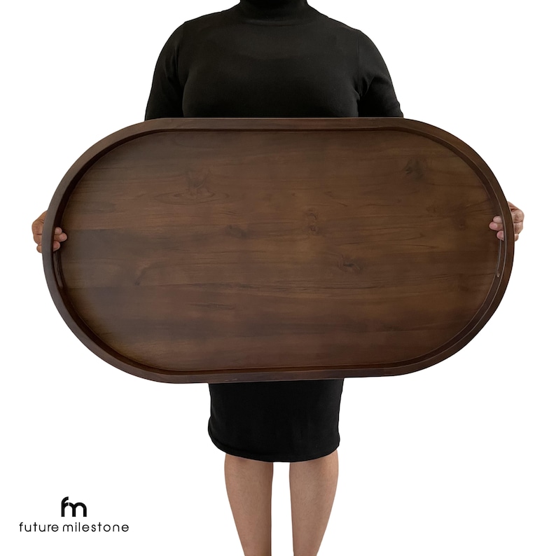 A large, oval-shaped wooden serving tray with a walnut finish. The tray is being held by a person to showcase you the perfect view of it.