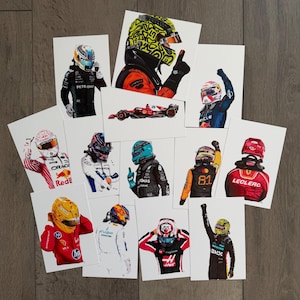 Könnte beinhalten: Eine Sammlung illustrierter Porträts von Formel-1-Fahrern, die ihre Helme und Rennanzüge zeigen. Die Kunstwerke zeigen verschiedene Fahrer, jeder mit einzigartigen Helmdesigns und Teamfarben, angeordnet auf einer Holzoberfläche.