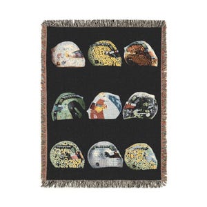 Könnte beinhalten: Eine schwarze Decke mit neun farbenfrohen Rennhelmen. Die Helme haben verschiedene Designs und Farben, darunter Weiß, Gelb, Grün und Silber. Die Decke hat einen Fransenrand.