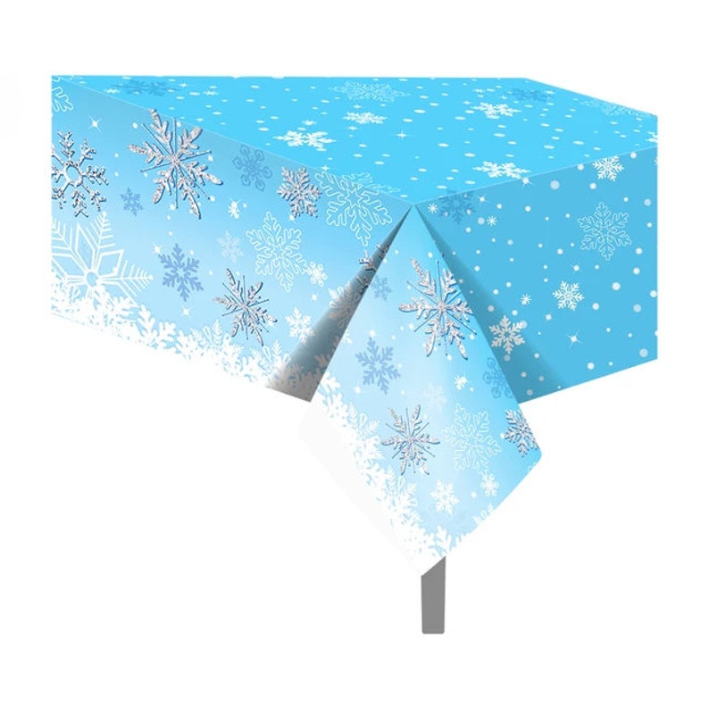 May include: A blue plastic tablecloth with a snowflake pattern. The tablecloth has a gradient of blue shades and features white snowflakes with silver glitter accents.